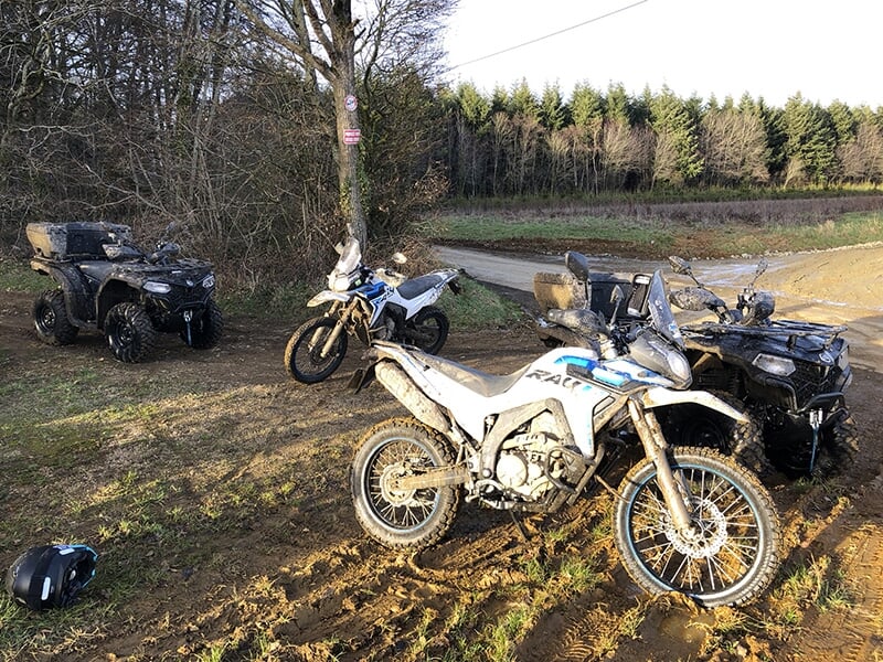Deux motos trail et deux quads à l'arrêt sur un chemin de terre avec une forêt en arrière-plan