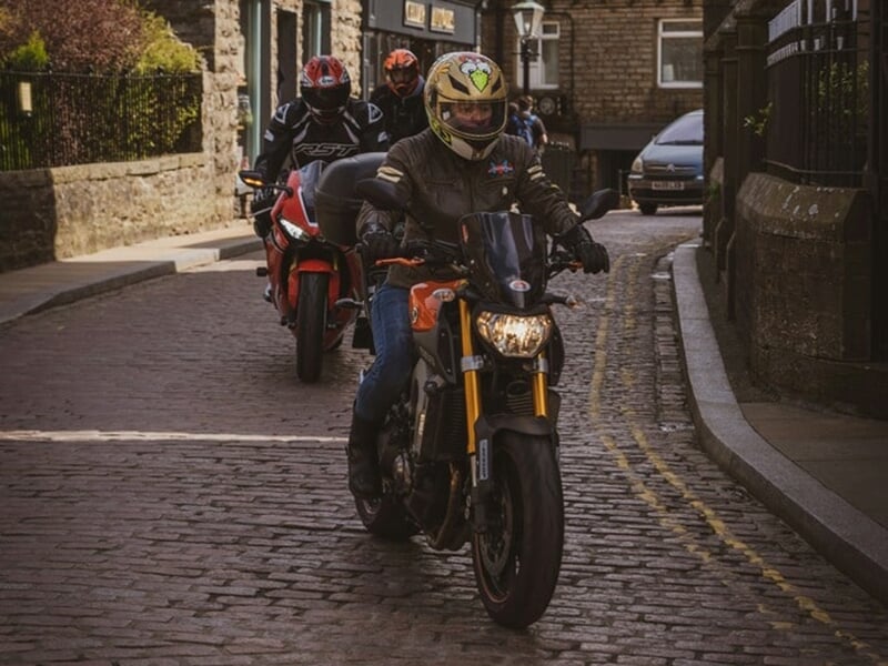 Groupe de motards en randonnée progressant sur une route pavée en ville