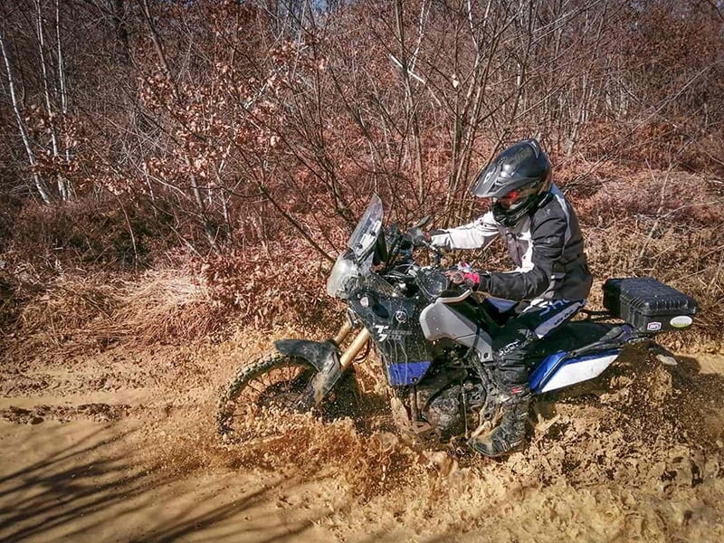 Motard sur une moto de trail en train de traverser un marre de boue dans une forêt 
