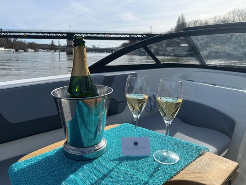 Une bouteille de vin pétillant dans un seau à champagne avec deux coupes pleines sur la table d'un bateau de croisière avec la Seine en arrière-plan