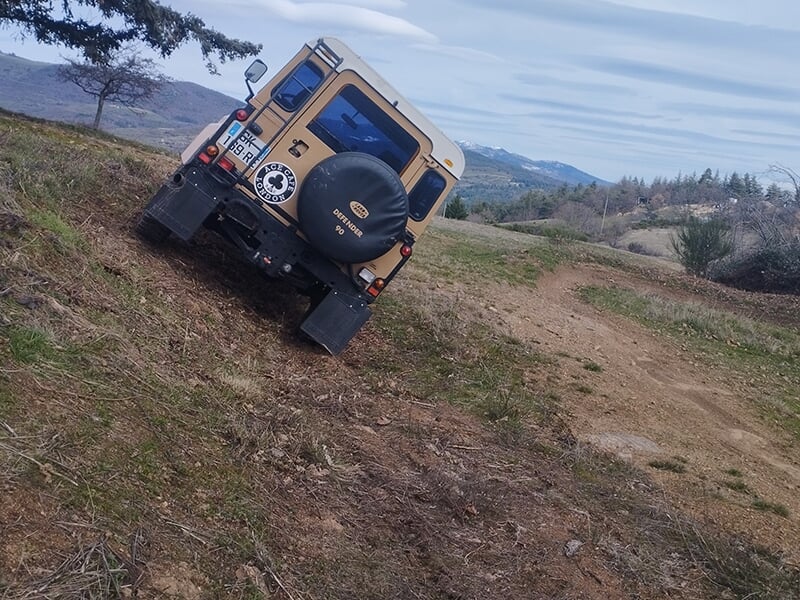 Gros plan sur l'arrière d'un véhicule 4x4 avec la roue de secours en train de monter une côte sur un terrain accidenté en plein au milieu de la nature. 