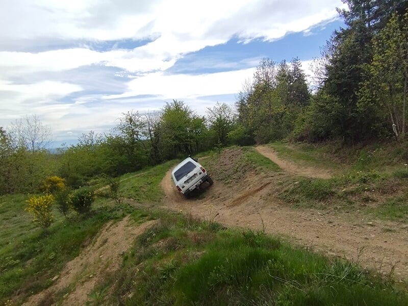 Un véhicule 4x4 de dos prend un dévers sur un chemin accidenté en pleine forêt