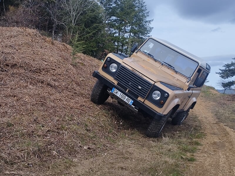Un 4x4 marron négocie un devers sur une piste de tout-terrain située en forêt