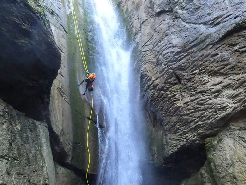 Canyoneur descendant en rappel une falaise à pic arrosé par une cascade vertigineuse