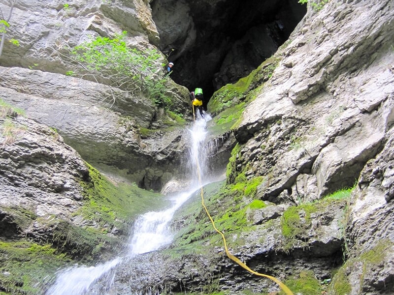 Fan de canyoning en plein milieu d'une descente en rappel sur une falaise escarpée des Alpes