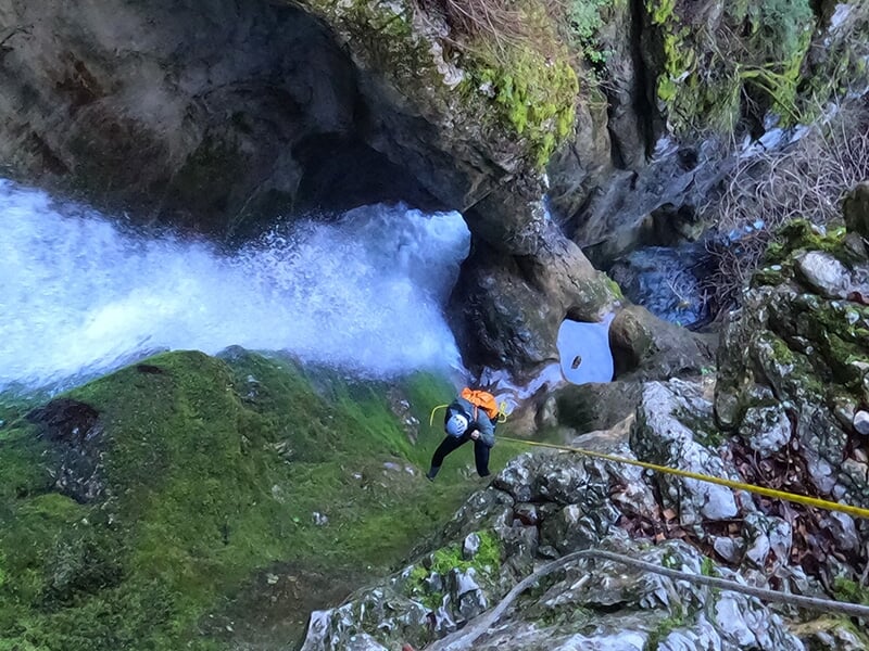 Canyoneur avec un sac à dos rouge effectuant une descente en rappel le long d'une cascade
