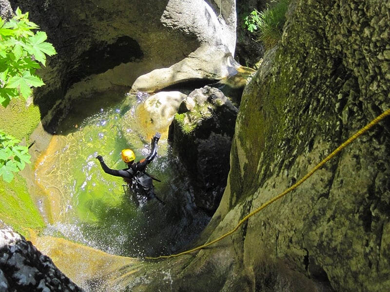 Un canyoneur fait un saut dans la vasque d'une cascade de montagne au cours d'une descente de canyon