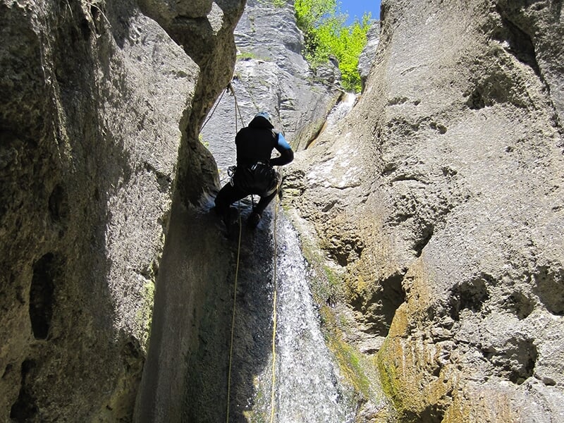 Un canyoneur de dos en plein milieu d'une descente en rappel sur une falaise érodée