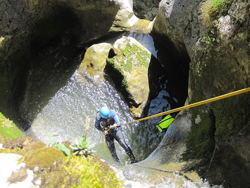 Un canyoneur vêtu d'une combinaison néoprène descend en rappel dans la vasque suspendue d'une cascade vertigineuse