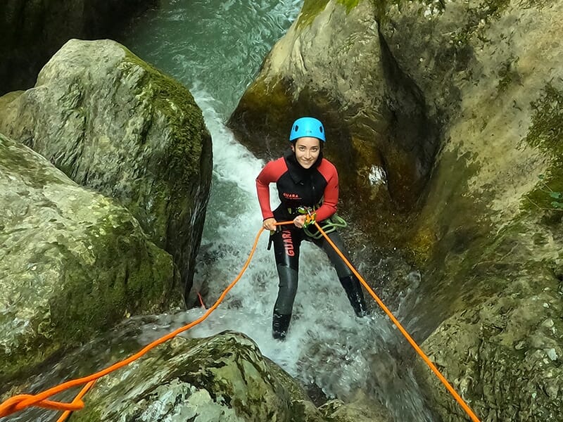 Une jeune femme descend en rappel une cascade escarpée dans un canyon de montagne