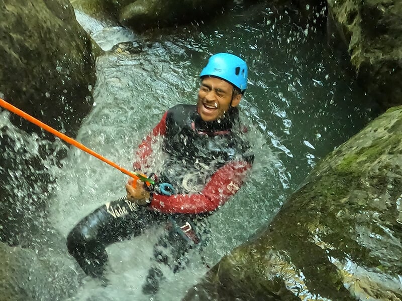 Un canyoneur vêtu d'une combinaison en néoprène et d'un casque bleu descend une cascade en rappel
