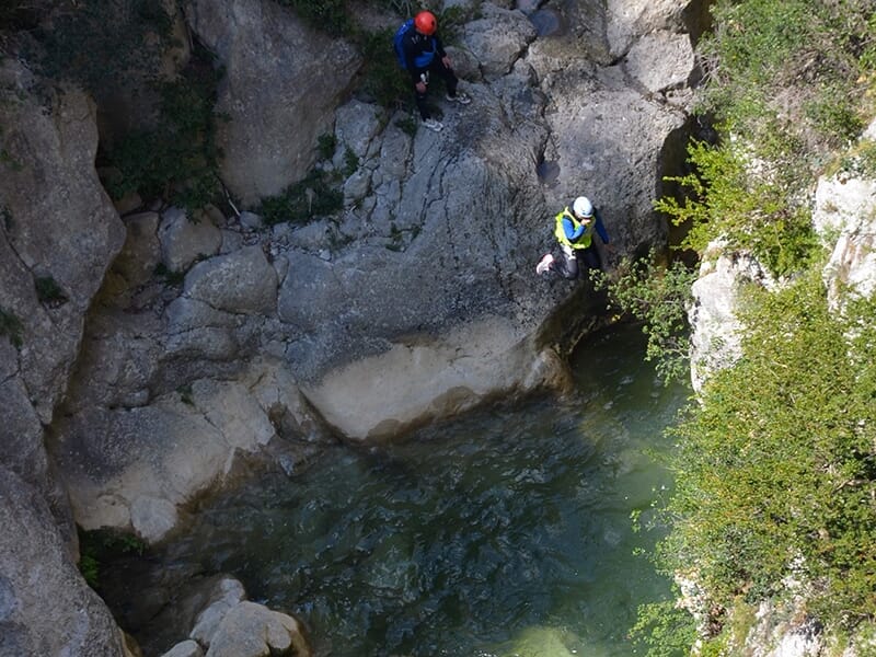 Un canyoneur équipé d'une combinaison en néoprène et d'un casque se tient debout au bord d'un torrent de montagne