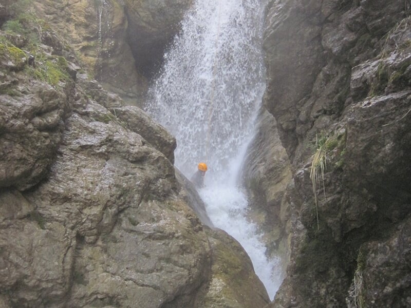 Un canyoneur progresse dans le lit d'une rivière de montagne tumultueuse lors d'une sortie de canyoning.