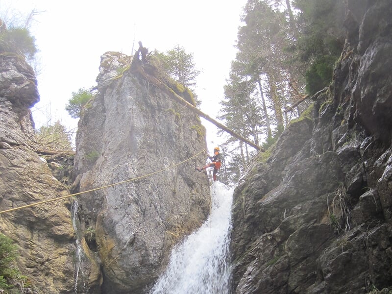 Un sportif entame une descente en rappel le long d'une cascade à fort débit lors d'une sortie de canyoning