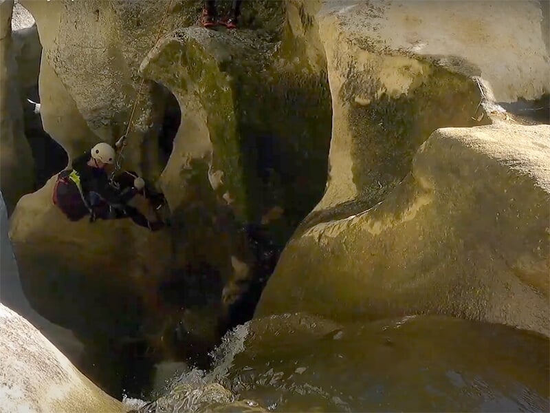 Un canyoneur portant un sac de canyon, un casque et une combinaison néoprène progresse dans une cavité souterraine