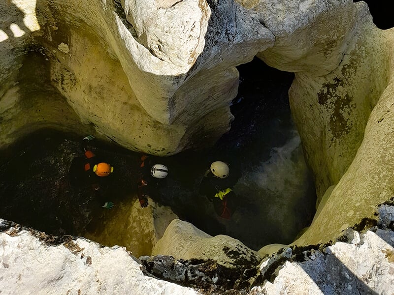 Des canyoneurs portant des casques progressent au fond d'une cavité rocheuse du canyon du Groin