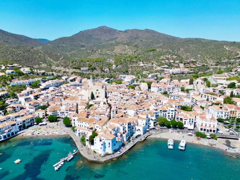 Vue aérienne de Cadaqués, une ville côtière pittoresque de Catalogne, avec ses maisons blanches aux toits en tuiles rouges bordant la mer Méditerranée. Collines verdoyantes à l'arrière-plan.