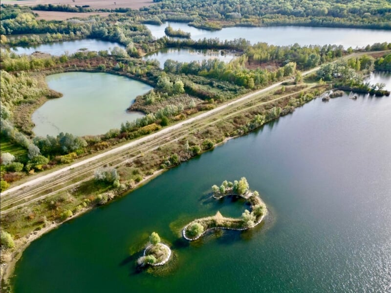 Vue aérienne d'un paysage de lacs et d'étangs interconnectés, entourés de végétation dense et de forêts. Une route traverse la scène, longeant les plans d'eau paisibles.