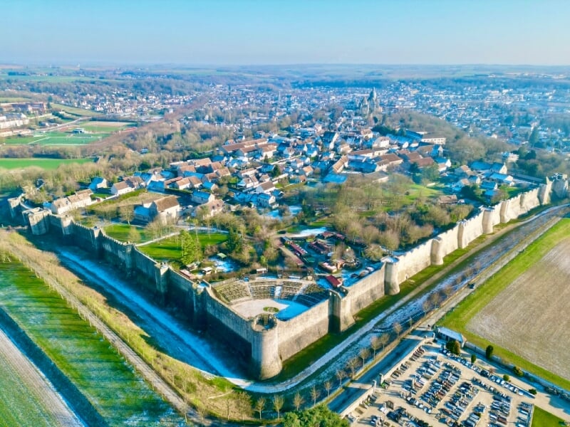Vue aérienne de la ville fortifiée de Provins, avec ses remparts médiévaux entourant les maisons et bâtiments historiques. Paysage rural et champs en arrière-plan.