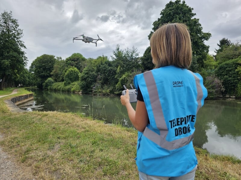 une personne de dos pilote un drone de loisir au bord d'une rivière