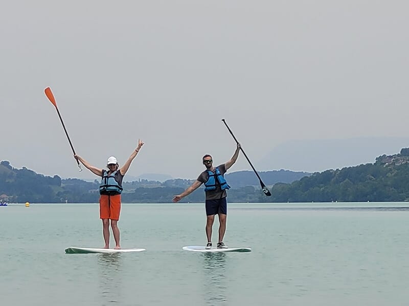 Des touristes équipés de gilets de sauvetage soulèvent leur pagaie debout un paddle sur un lac avec des collines en arrière-plan