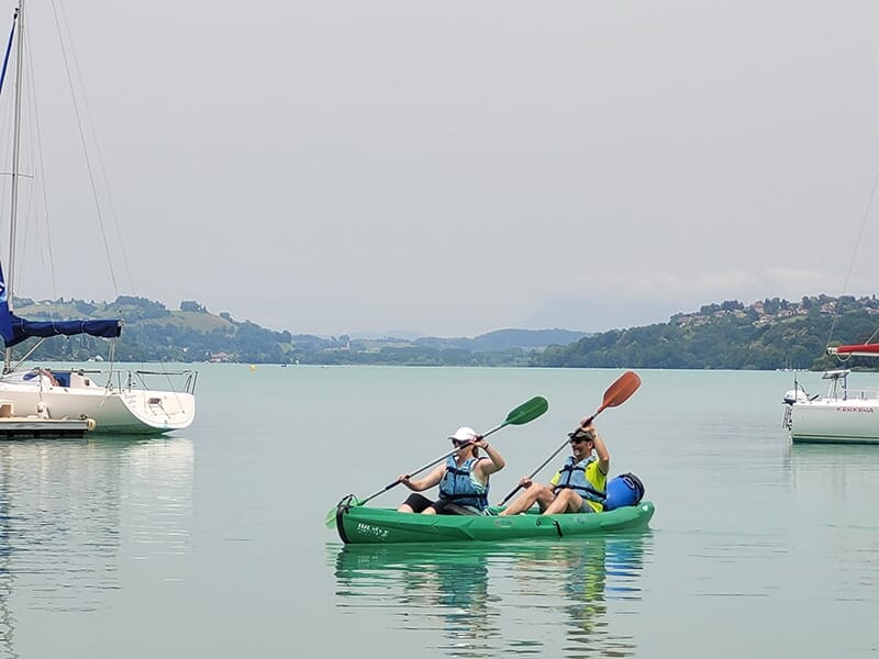 Un couple de touristes portant des gilets de sauvetage rament dans un canoë sur un lac naturel avec des montagnes en toile de fond