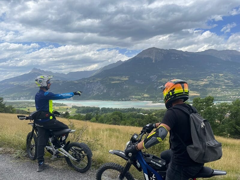 Un guide à moto montre un point d'intérêt à un stagiaire avec un lac bleu azur en toile de fond