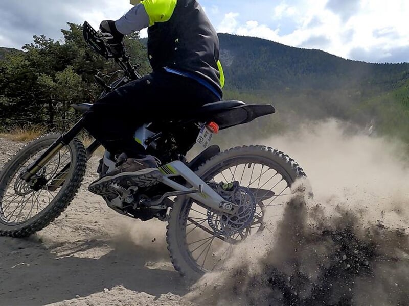 Un motard fait de la moto-cross sur un chemin de terre et soulève de la poussière avec la roue arrière.