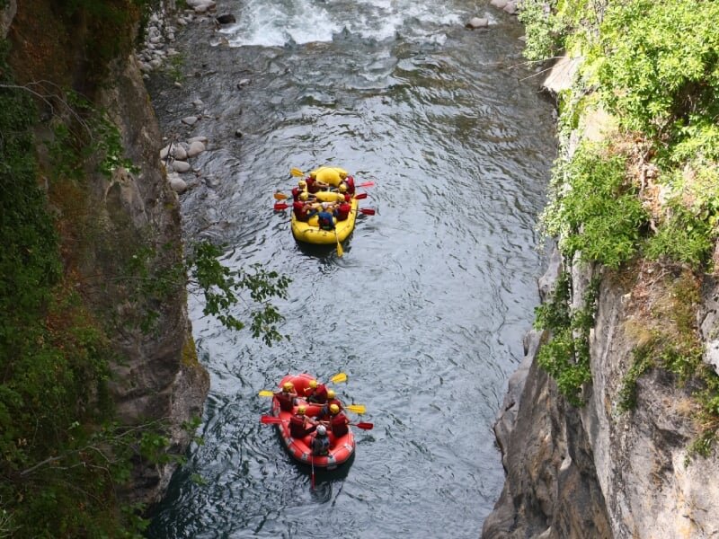Vue aérienne de deux radeaux de rafting descendant une gorge étroite et sinueuse. Le premier radeau est jaune et le second rouge, chaque groupe pagayant vigoureusement. Les radeaux sont entourés de fa