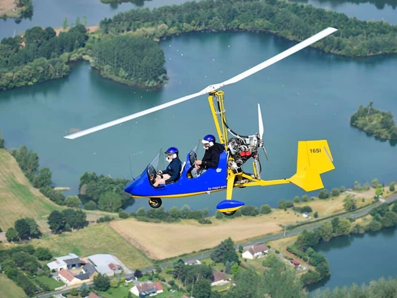 ULM bleu en vol au-dessus d'un paysage rural avec des plans d'eau et des champs verts.