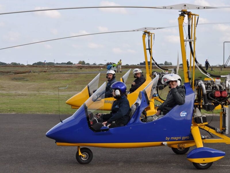 ULM bleu au sol avec plusieurs personnes à bord et autour, sur une piste d'aviation.