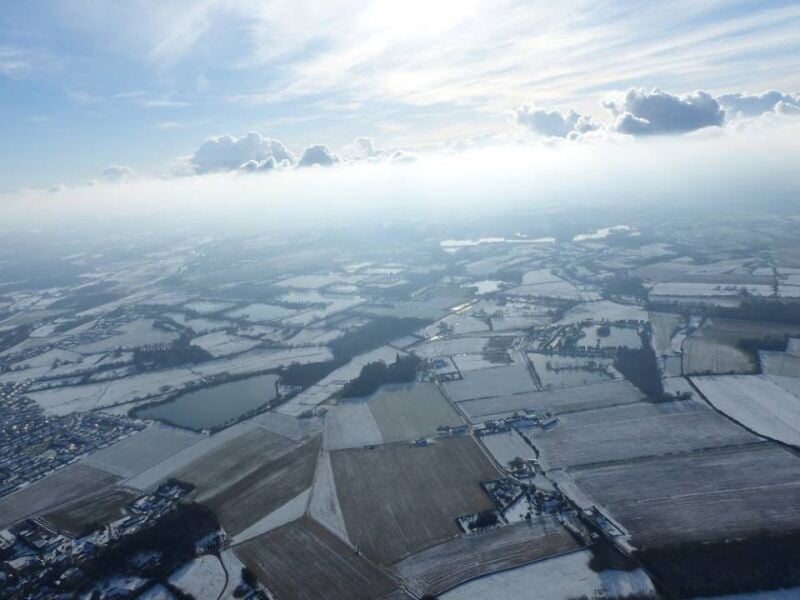 Vue aérienne d'un paysage hivernal avec champs enneigés et villages sous un ciel nuageux.