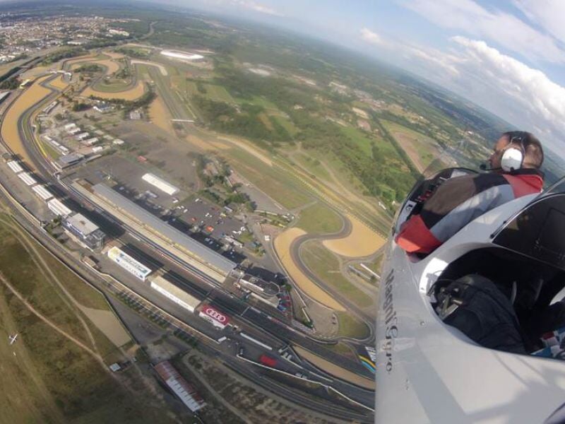 Vue aérienne d'un circuit automobile avec des bâtiments et des routes, prise depuis un ULM.
