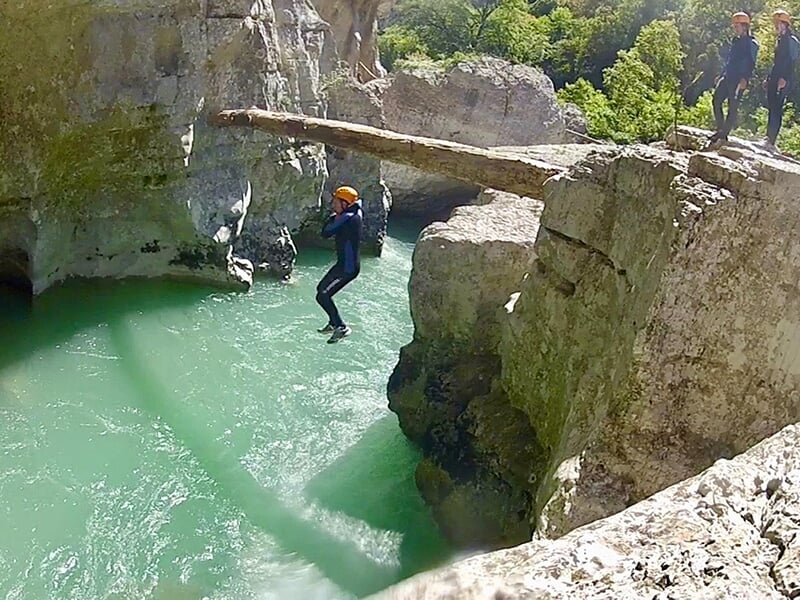 Un adepte du canyoning fait un saut spectaculaire dans un torrent alors que les autres stagiaires attendent leur tout pour sauter perchés sur un rocher