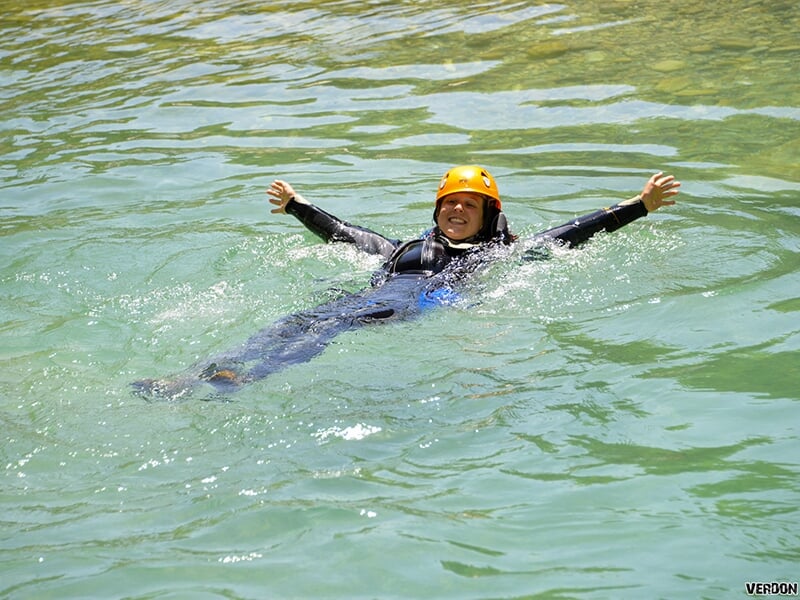 Une jeune femme souriante pratiquant le canyoning nage dans l'eau bleu d'un torrent en agitant les bras
