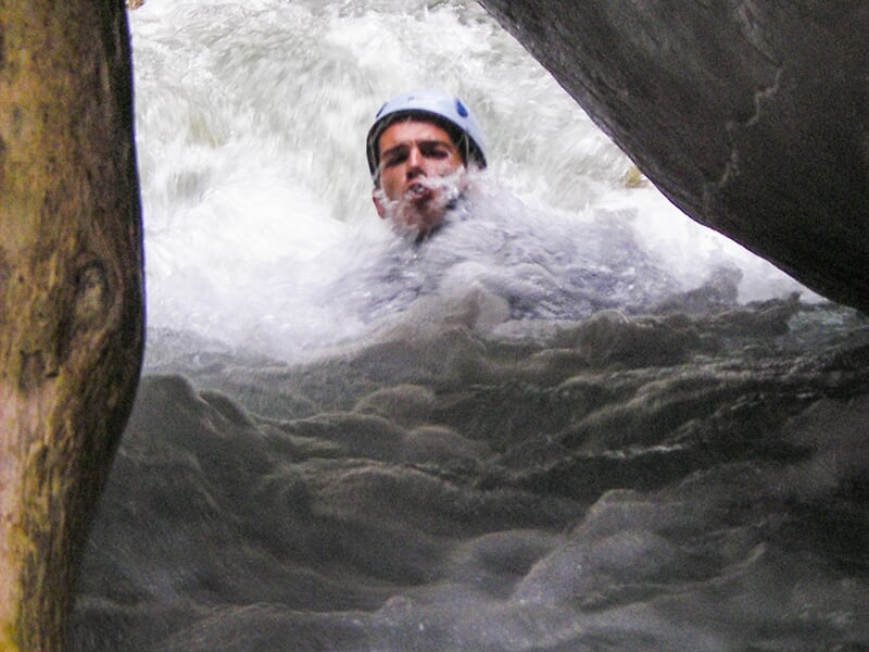 Jeune homme portant un casque descendant les rapides du verdon en passant sous un rocher