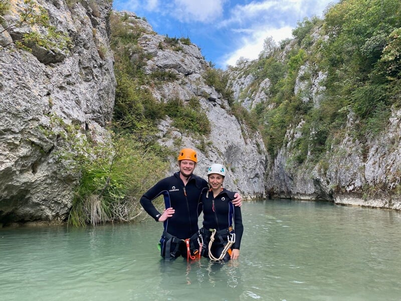 Deux personnes en tenue de canyoning posent pour la photo les pieds dans l'eau au cours d'une randonnée aquatique avec des falaises en toile de fond