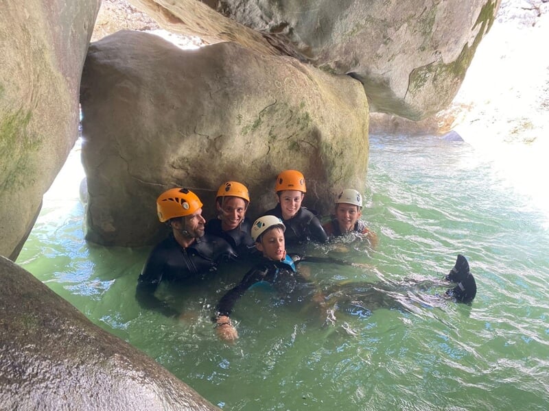 Un groupe de randonneurs aquatiques  en combinaison néoprène se reposent près d'un gros rocher dans une rivière de montagne