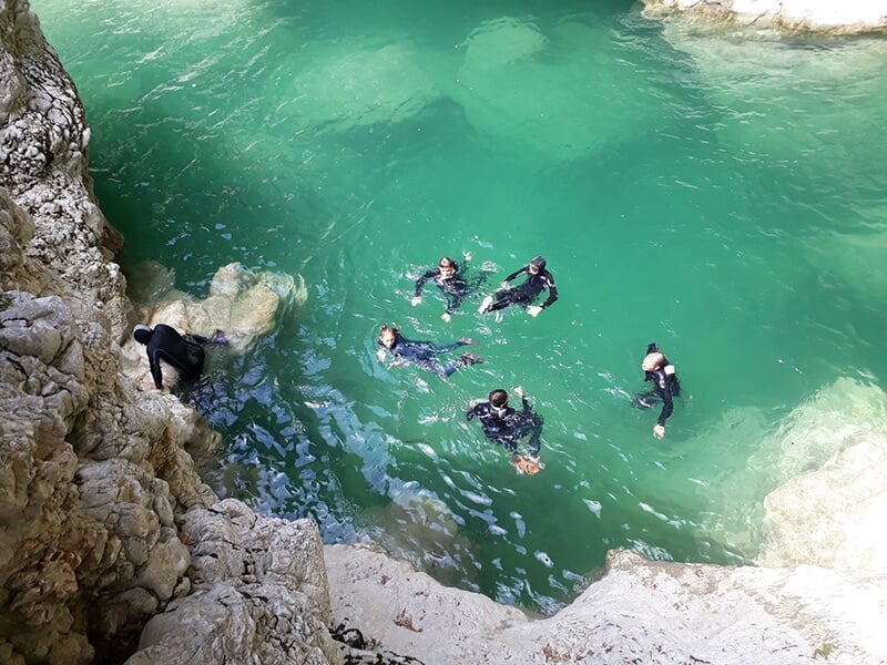 Un groupe de canyoneurs en train de nager dans un torrent au pied d'une falaise vertigineuse
