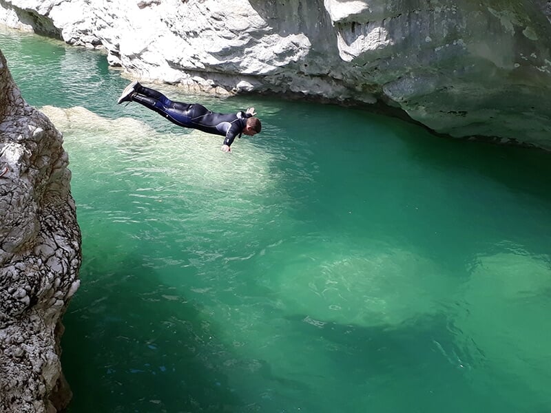 Un homme portant une combinaison néoprène plonge la tête la première dans les eaux bleutés d'un torrent