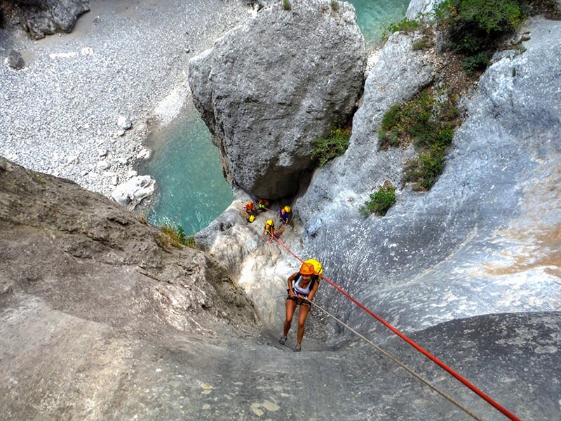 Une femme vêtue d'un short descend en rappel une paroi vertigineuse avec en toile de fond une rivière de montagne