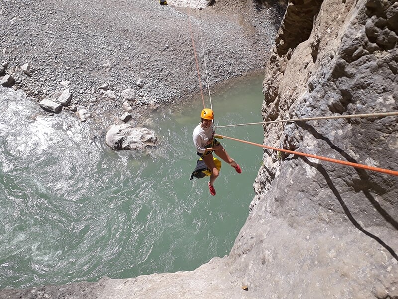 Un randonneur effectue une descente en rappel le long d'une falaise escapée au-dessus d'une rivière de montagne.