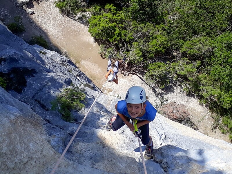 Une jeune fille regarde l'objectif du photographe en plein milieu d'une descente en rappel sur une falaise escarpée