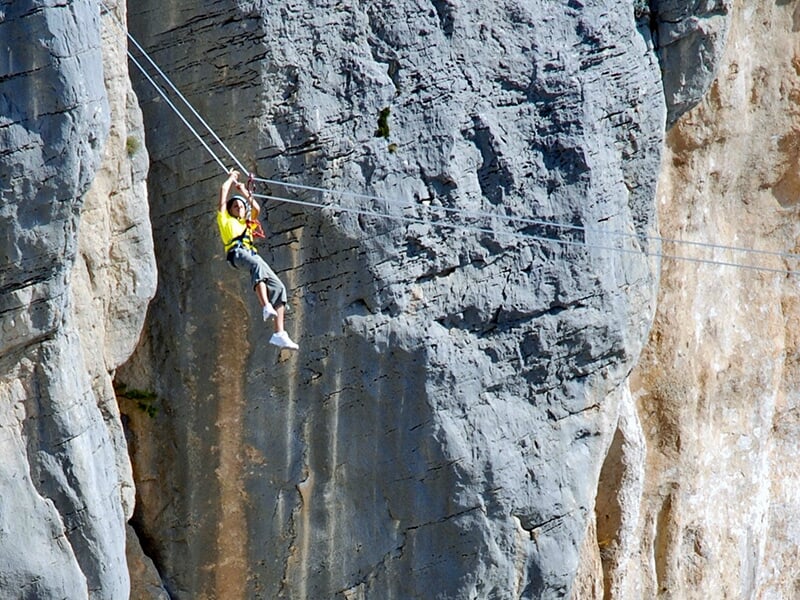 Jeune femme vêtue d'un tee-shirt jaune fait une descente en tyrolienne avec une falaise calcaire en arrière-plan