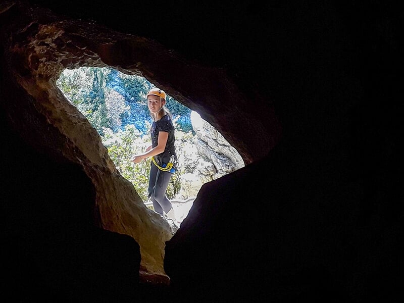 Jeune fille équipée d'un baudrier pose dans l'embrasure d'une grotte creusée dans la roche calcaire des gorges du Verdon