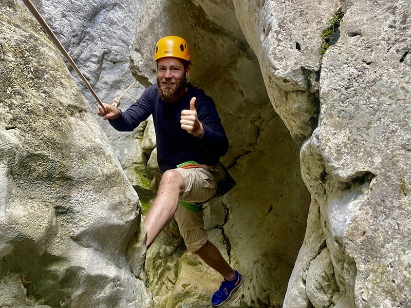Un grimpeur portant un casque de protection jaune tend le pouce en signe de satisfaction en plein milieu d'une paroi rocheuse