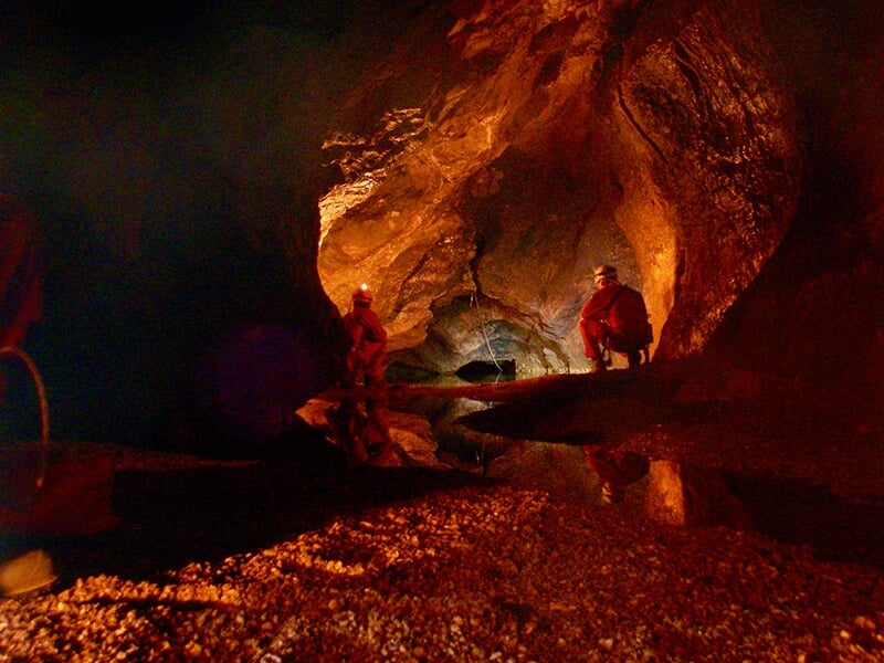 Deux spéléologues avancent dans une grotte traversée par une rivière souterraine