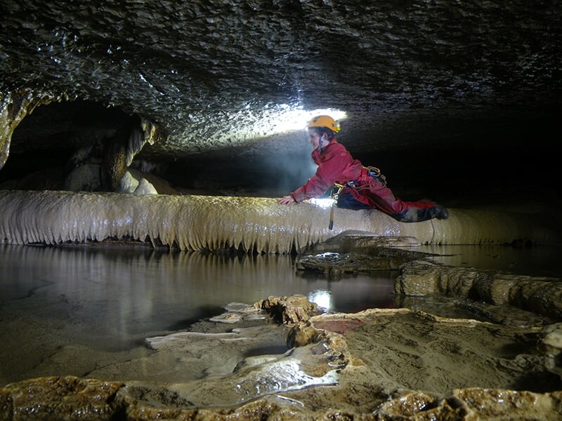 Un enfant pratiquant la spéléologie progresse dans une grotte éclairé d'une lampe frontale