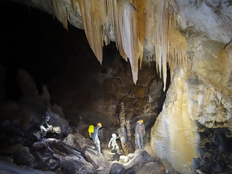 Un groupe de spéléologues progressent dans une cavité souterraine sous un plafond de stalactites