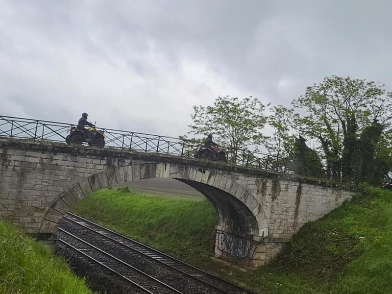 Un quad traverse un pont qui enjambe une voie ferrée en pleine campagne